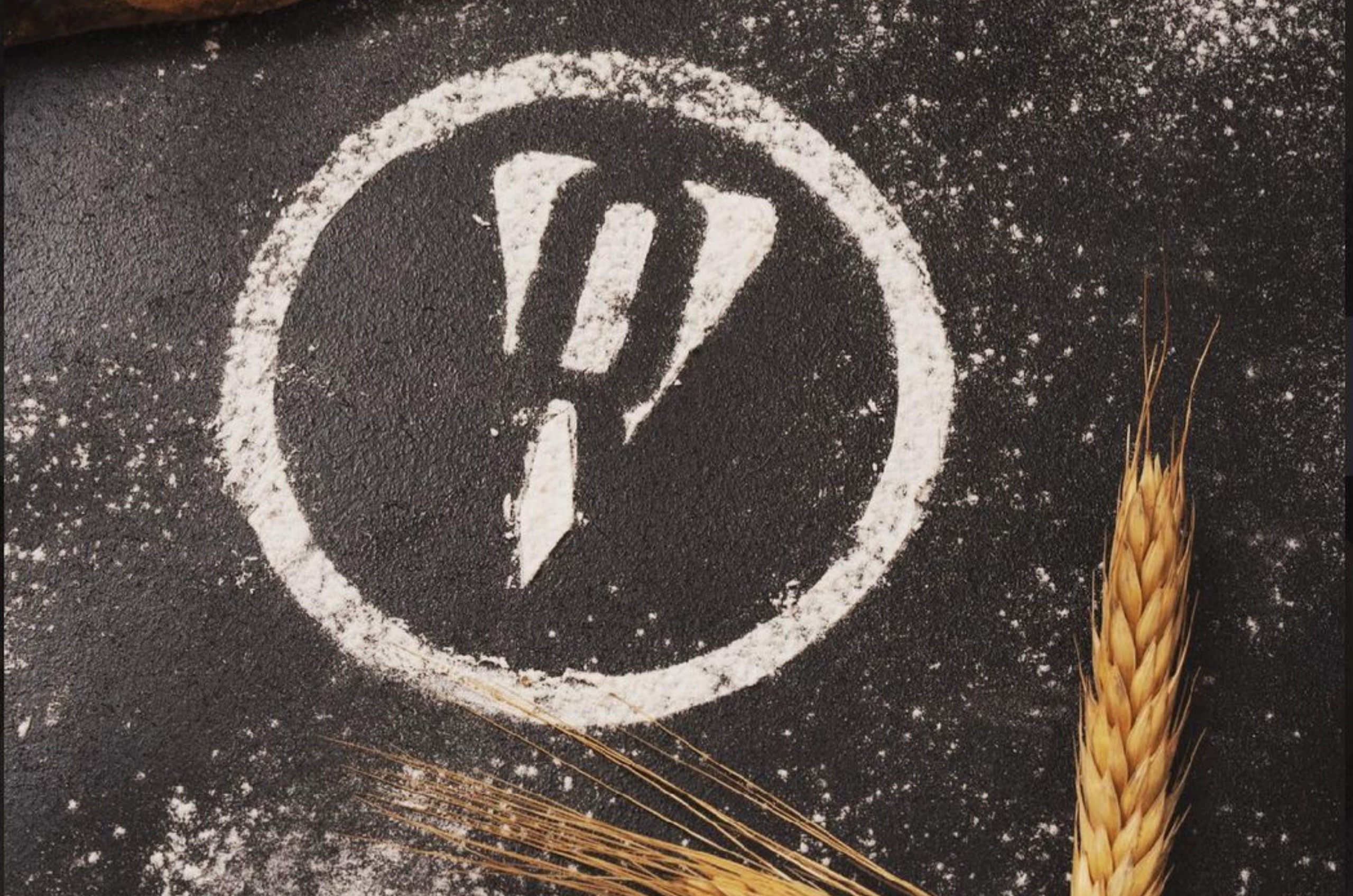 Pizza Rubato company logo made of white flour near a stalk of wheat on a black background