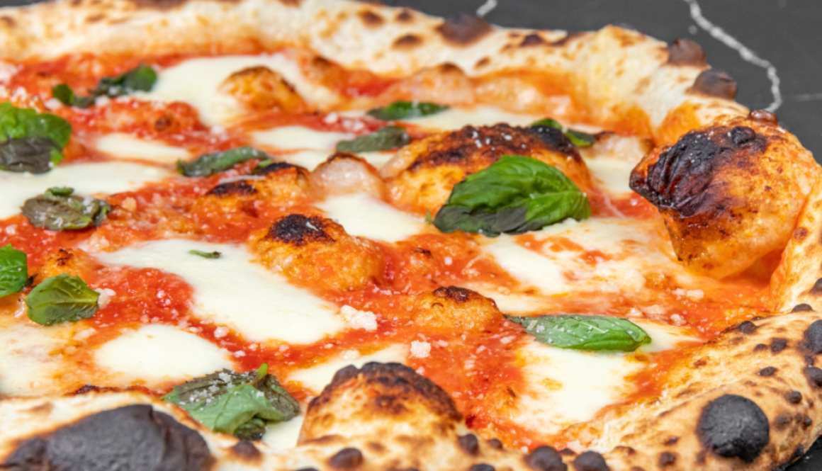 A freshly baked Neapolitan pizza with charred crust, tomato sauce, mozzarella cheese, and fresh basil leaves