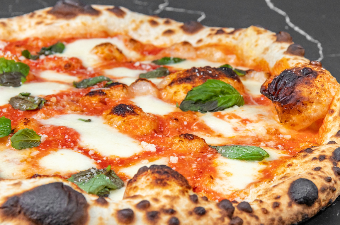 A freshly baked Neapolitan pizza with charred crust, tomato sauce, mozzarella cheese, and fresh basil leaves